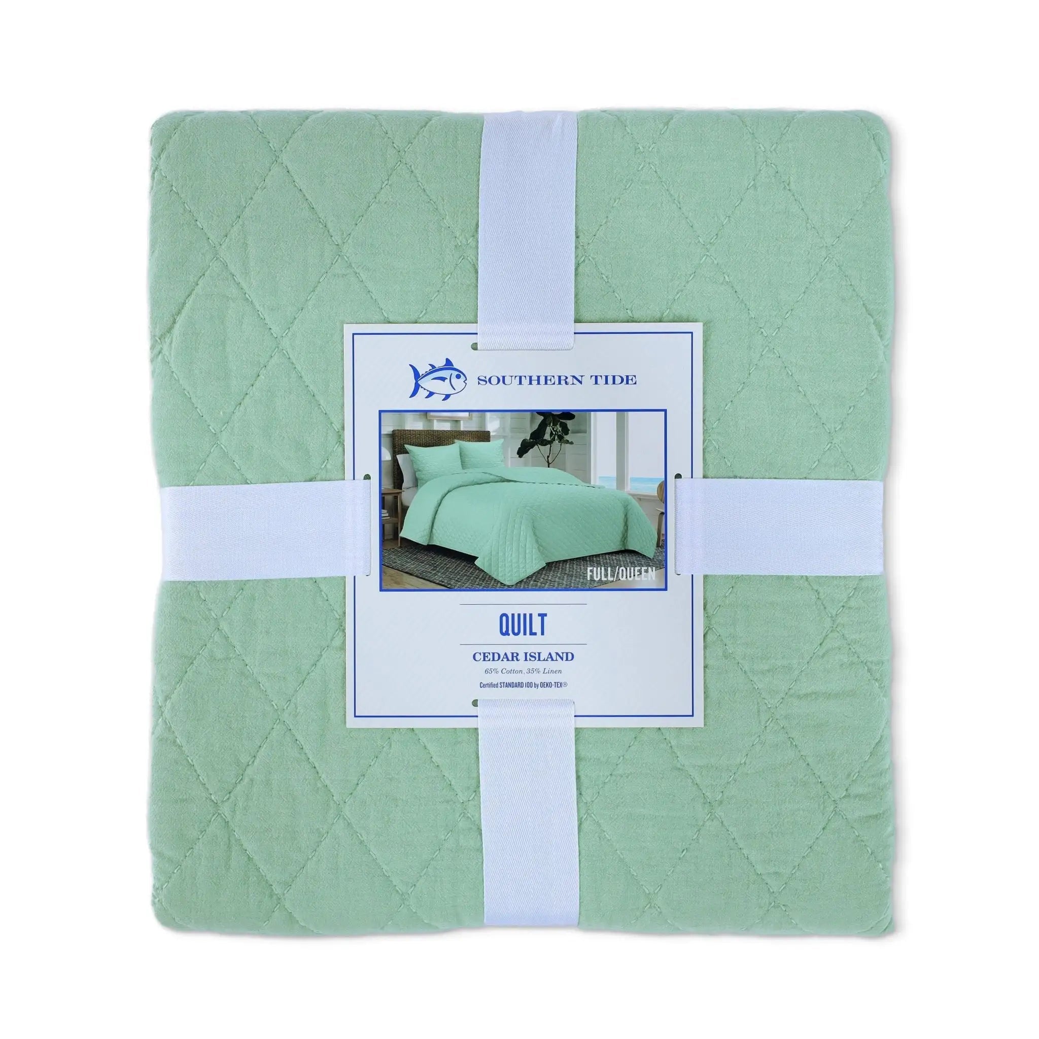 A folded sage green quilt wrapped in a white ribbon with a central paper label that reads Southern Tide Quilt Cedar Island.