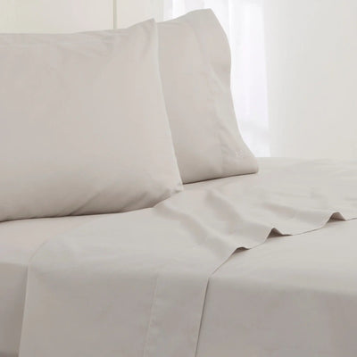 Grey cotton sheet and pillowcase set on a bed, with two pillows and a neatly draped sheet in a bright, clean bedroom setting.