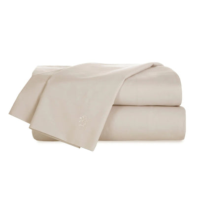 A folded bed sheet set in a light cream or ivory color, featuring a small embroidered monogram logo on the corner, set against a plain white background.