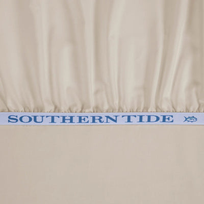 Close-up of a cream-colored fabric product, likely a bedspread or sheet, gathered at the top edge with a light blue elastic band featuring the brand name 'SOUTHERN TIDE' in blue text and a small fish logo.