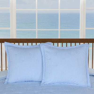 Two light blue euros displayed on a bed with a wooden headboard, set against a large window with an ocean view.
