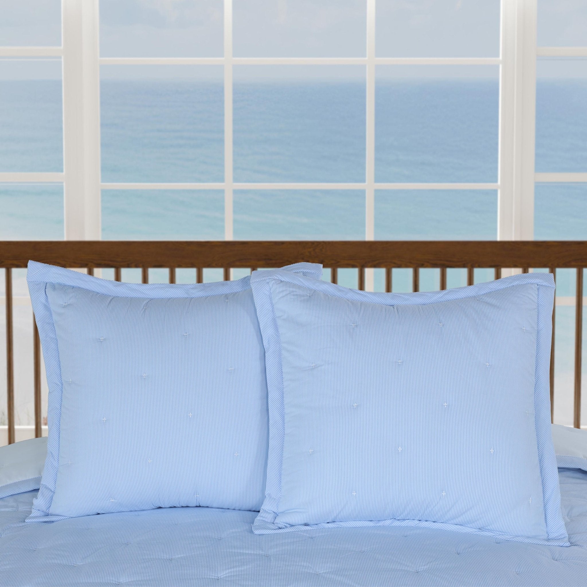 Two light blue pillows on a bed with a window in the background