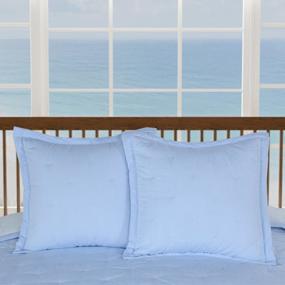 Two light blue pillows on a bed with a window in the background