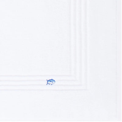 A close-up of a white bath mat surface, with a small blue fish emblem near the bottom edge.