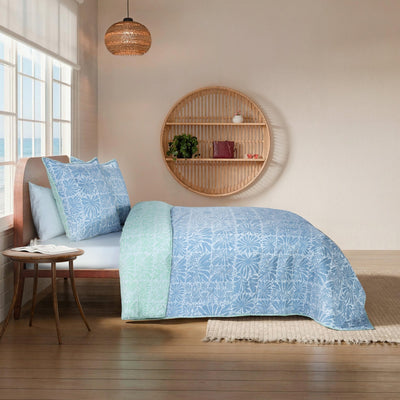 Bed with blue and green floral-patterned bedding in a room.