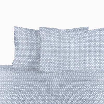 A close-up of a bed sheet with two matching pillowcases, featuring a repeating geometric pattern in light blue and white.