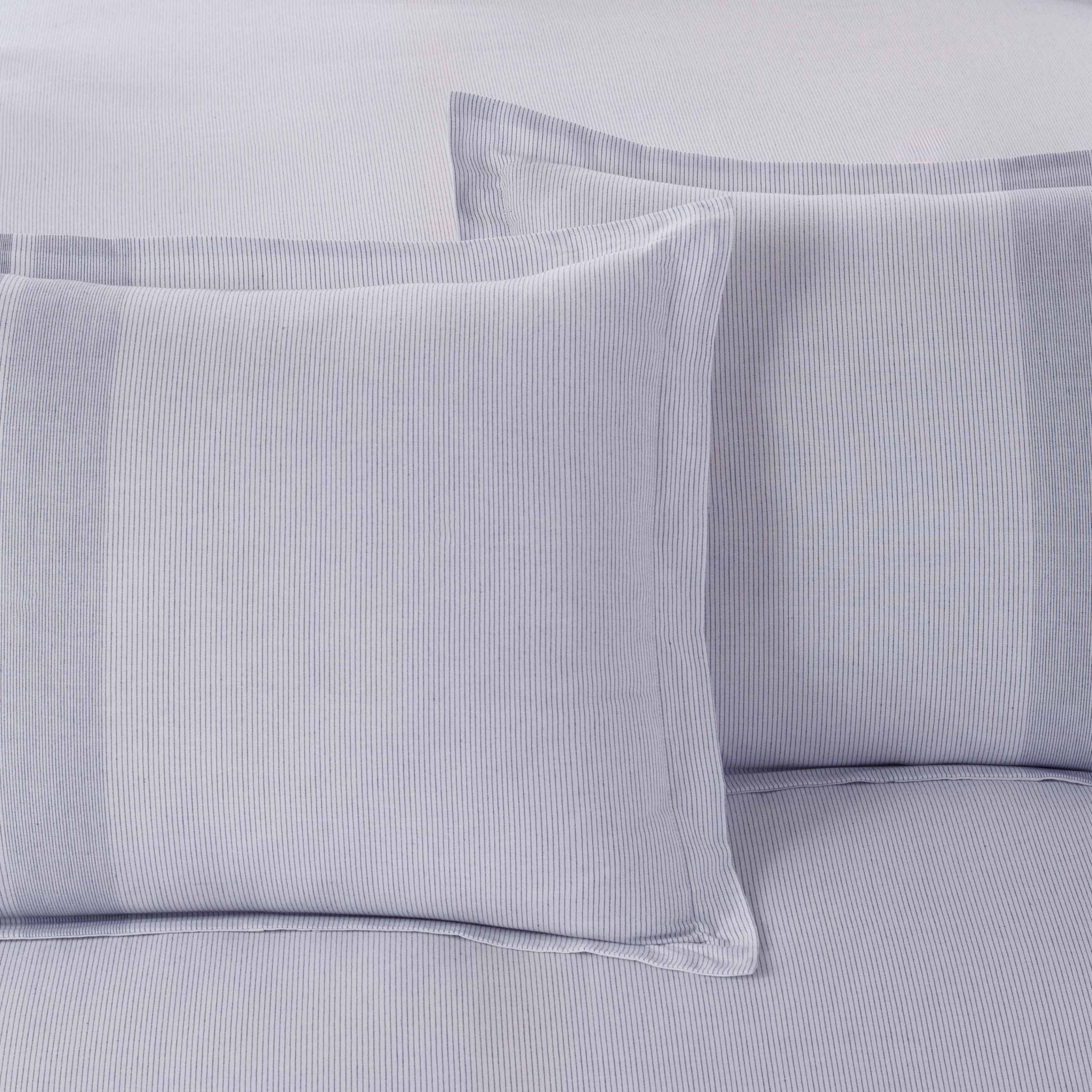 Close-up of light blue striped bedding with pillow shams on a matching fabric background