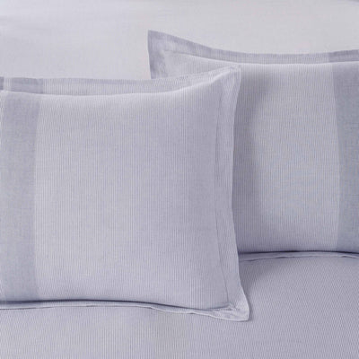 Close-up of light blue striped bedding with pillow shams on a matching fabric background