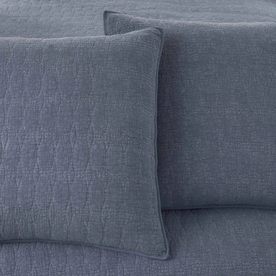 A close-up of a slate blue quilt featuring a textured pillow sham.