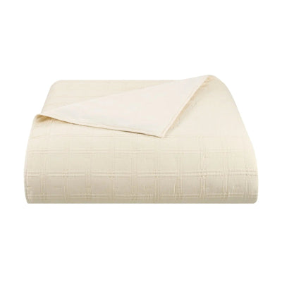 An ivory quilt with a subtle grid pattern, folded neatly with one corner folded over, shown on a solid white background.