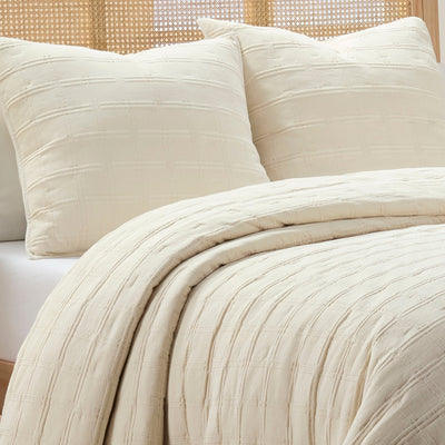 Beige textured quit and euros on a bed with a woven headboard.