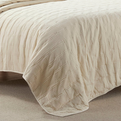 Beige textured quilt draped over a bed on a neutral background