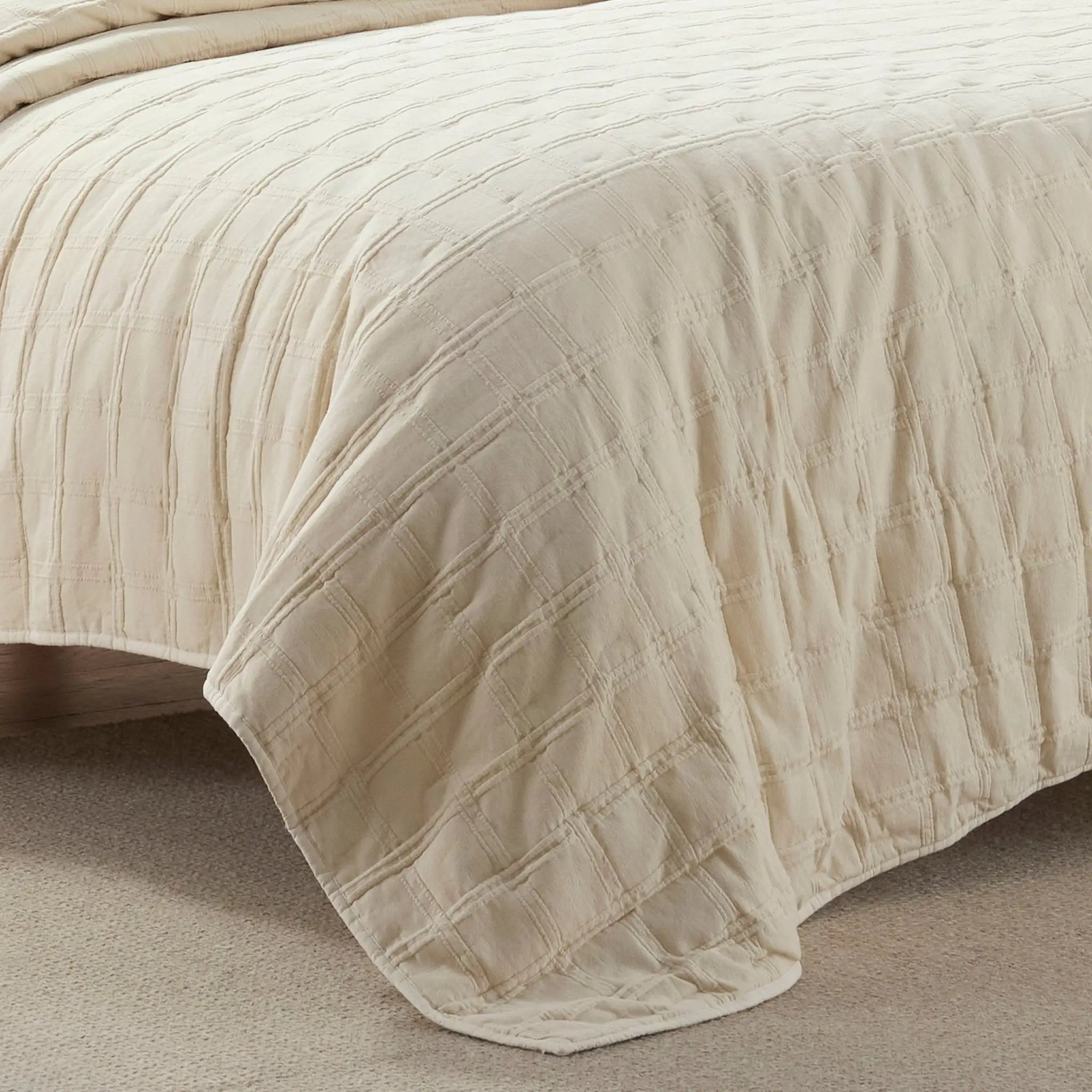 Ivory textured quilt draped over a bed on a neutral background