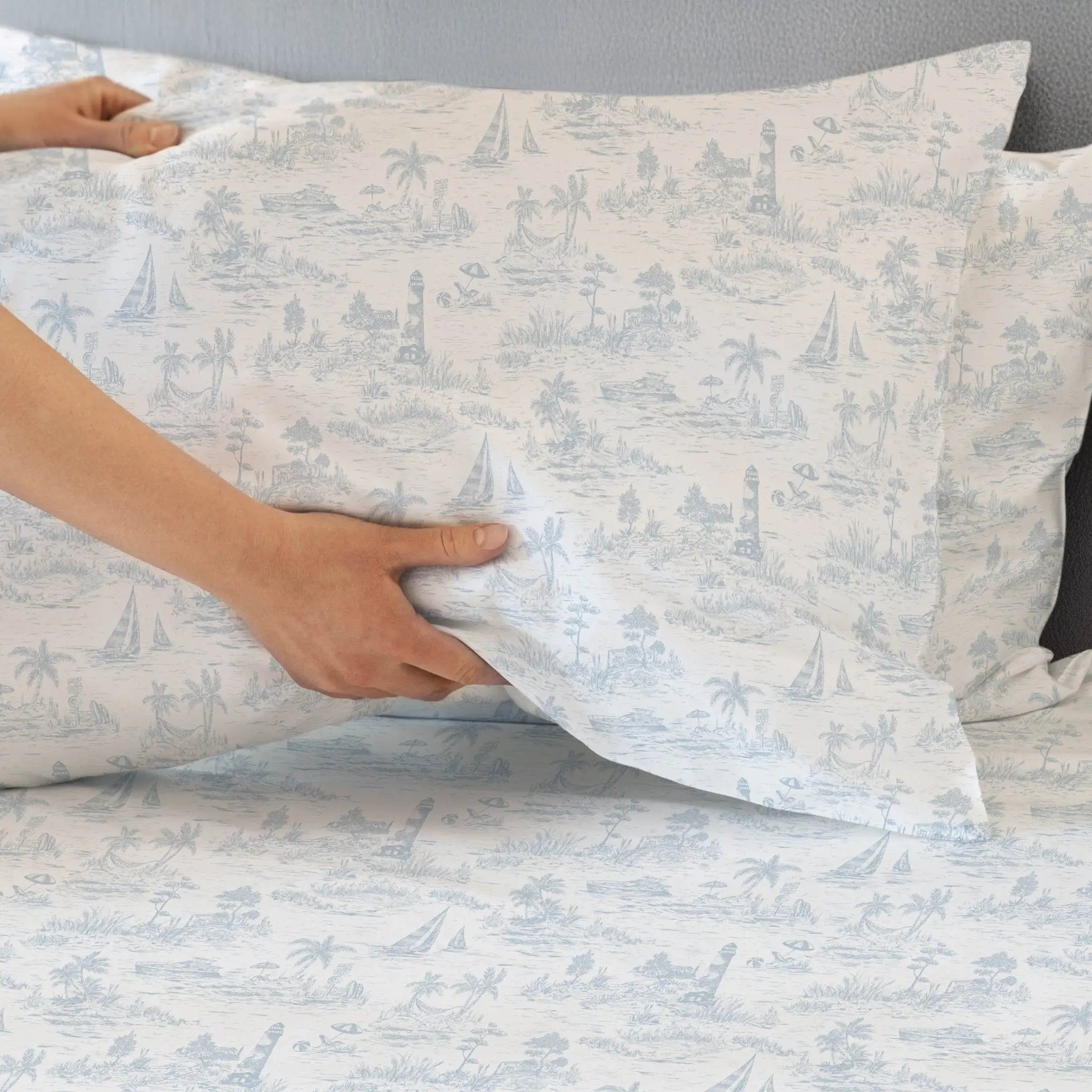 Person holding a pillow with a blue and white pattern on a bed