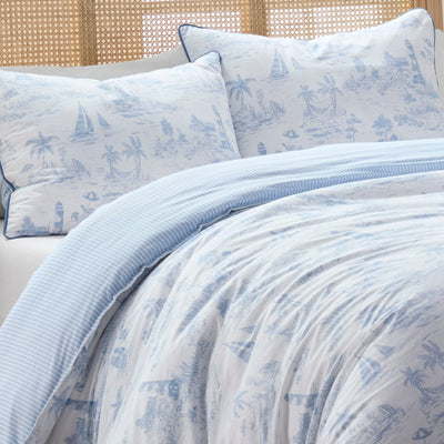Blue and white patterned bedding set on a bed with a woven headboard.