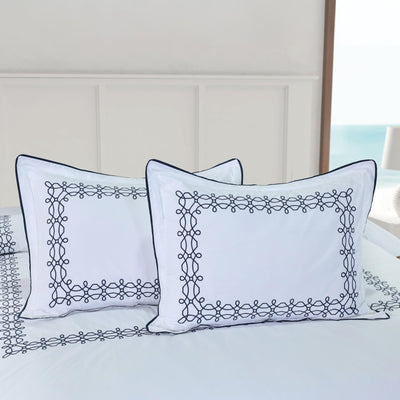 Two white shams with black embroidery on a bed.