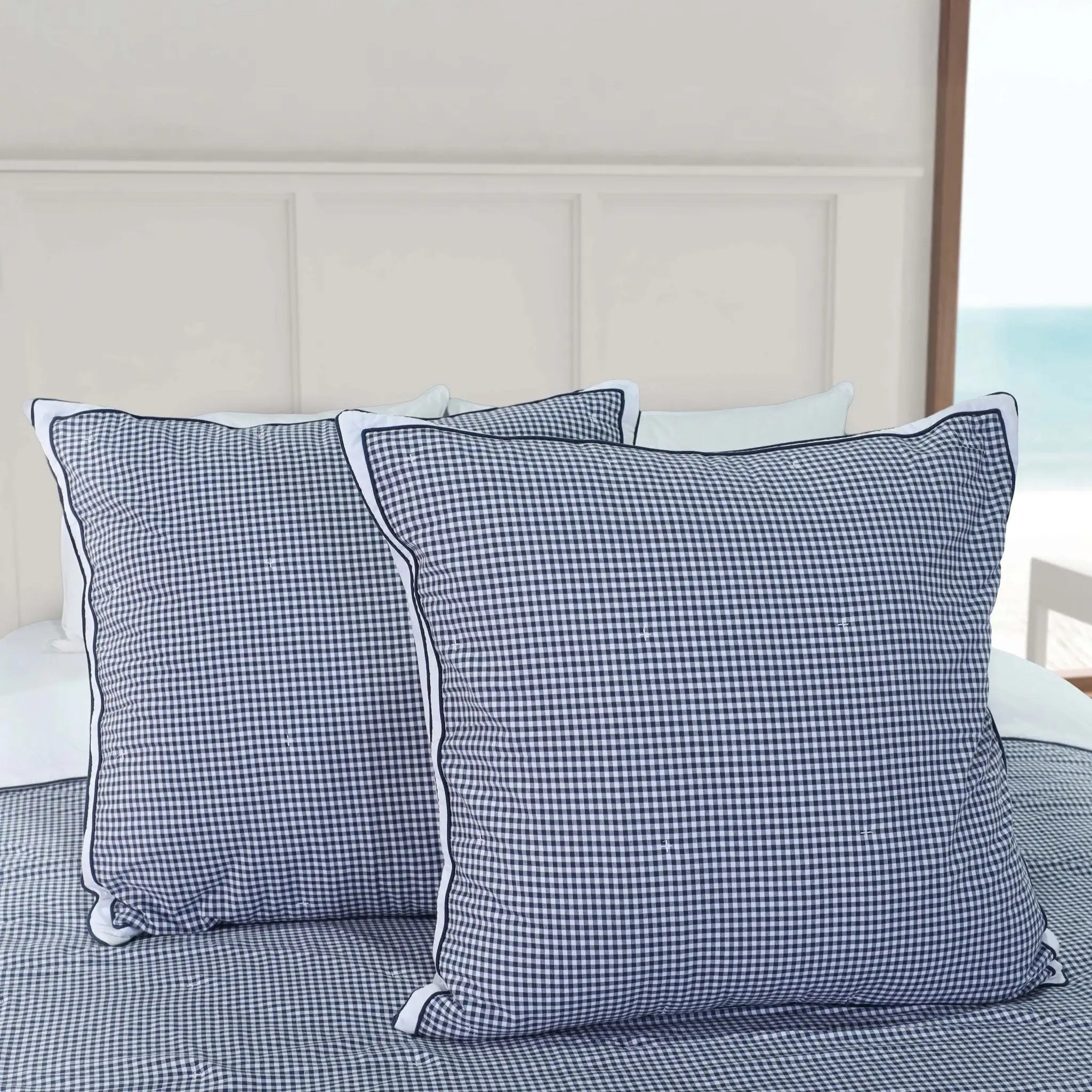 Two blue checkered euros on a bed with a neutral headboard.