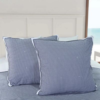 Two blue checkered euros on a bed with a neutral headboard.