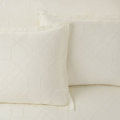 Close-up of ivory quilted comforter with pillow shams on a neutral background