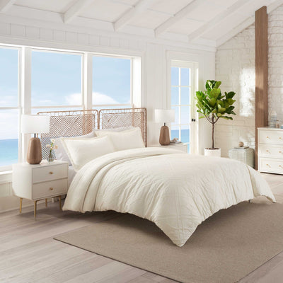 Neatly made bed with ivory comforter set in a bright bedroom.