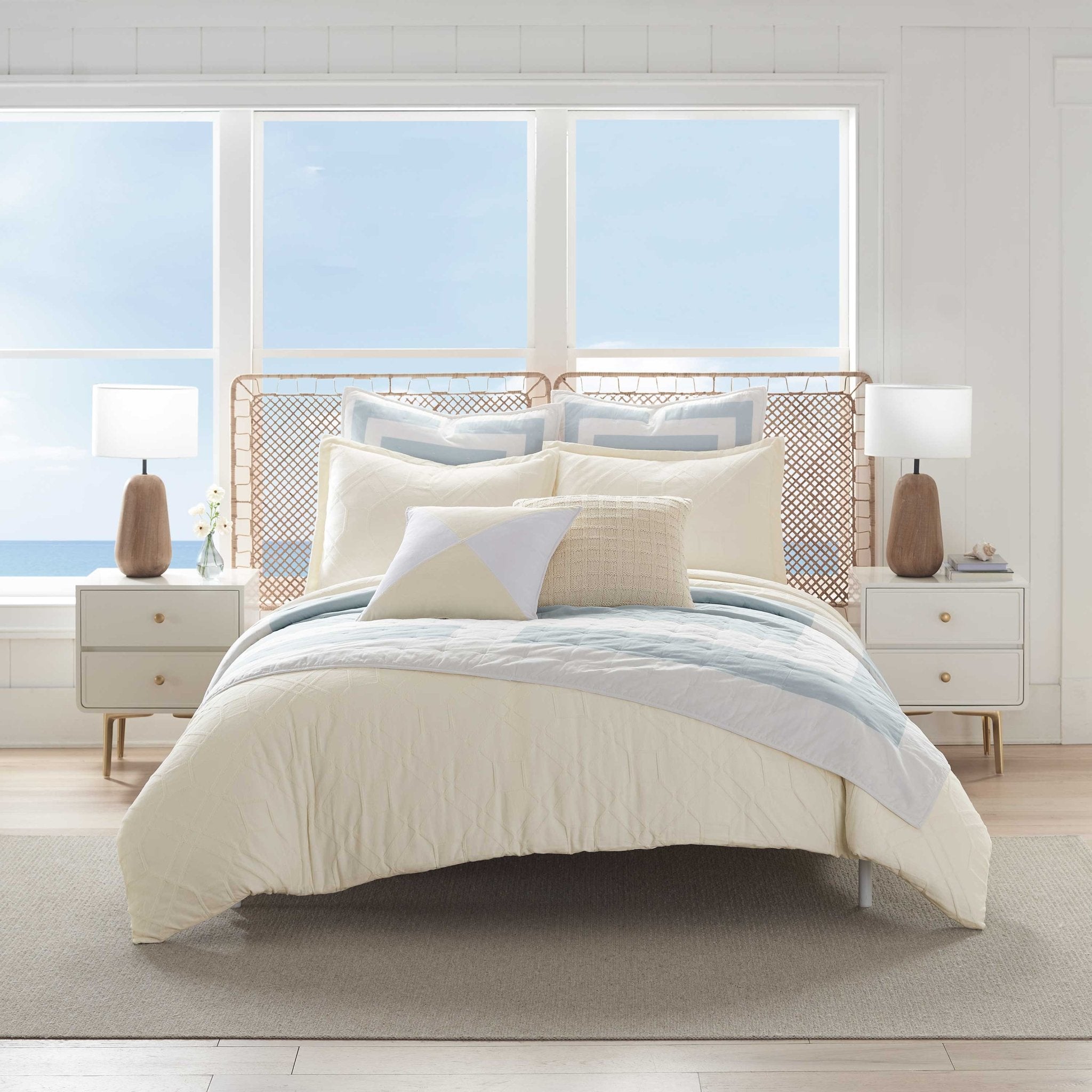 Neatly made bed with light-colored comforter set in a bright bedroom.
