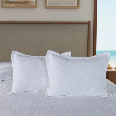 Two white pillow shams on a bed with a neutral headboard.