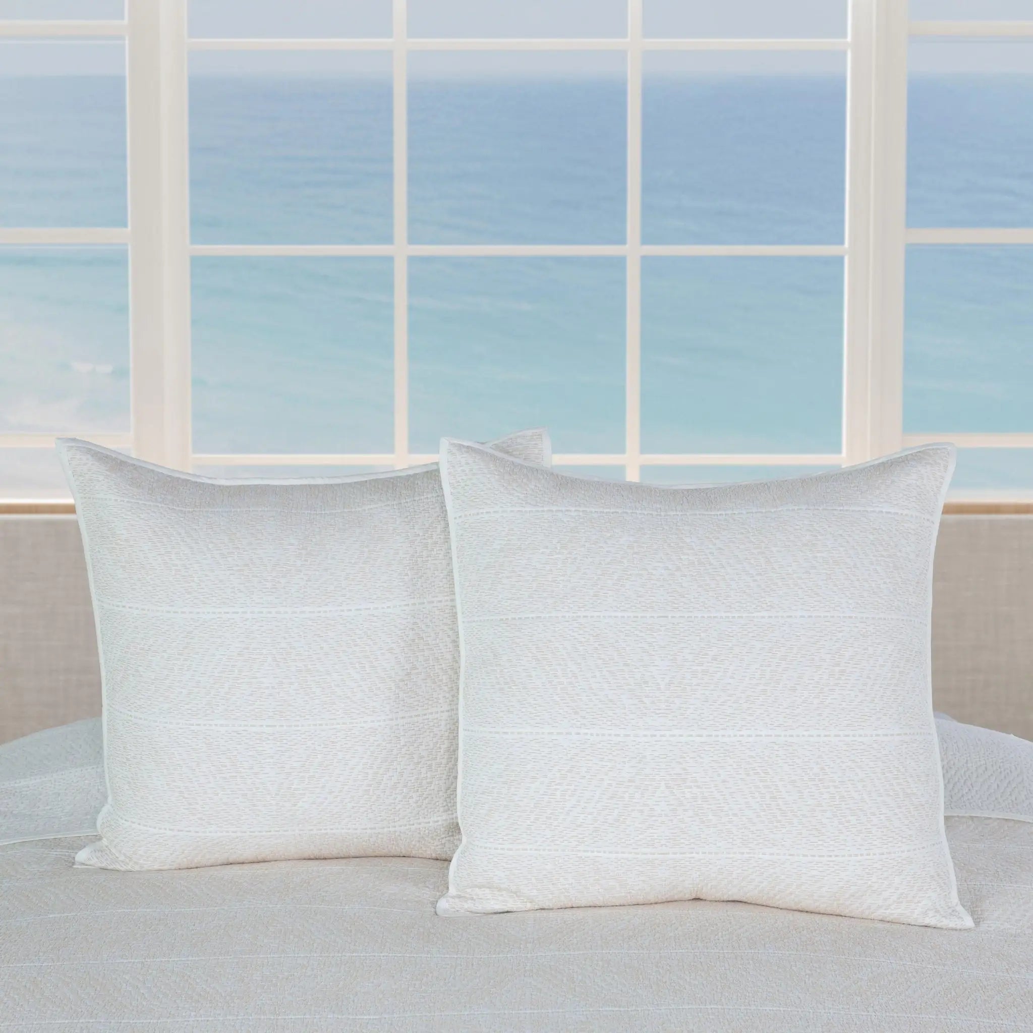 Two square white textured euros resting on a light beige bed.