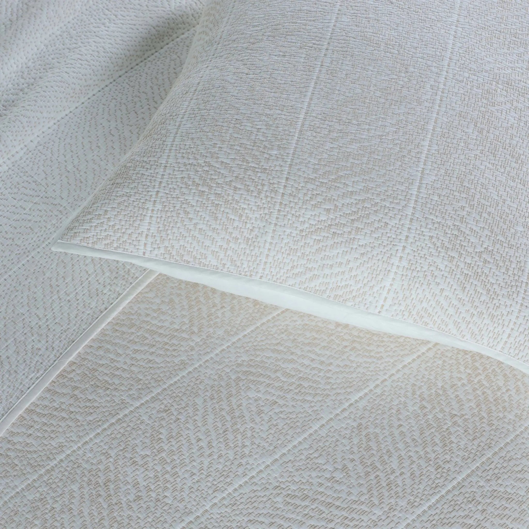 A close-up of a textured white euros and matching white quilted bedding, showing a fine woven pattern and subtle stitched channel details.