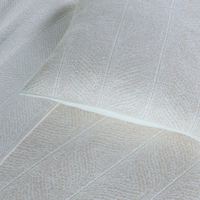 A close-up of a textured white euros and matching white quilted bedding, showing a fine woven pattern and subtle stitched channel details.