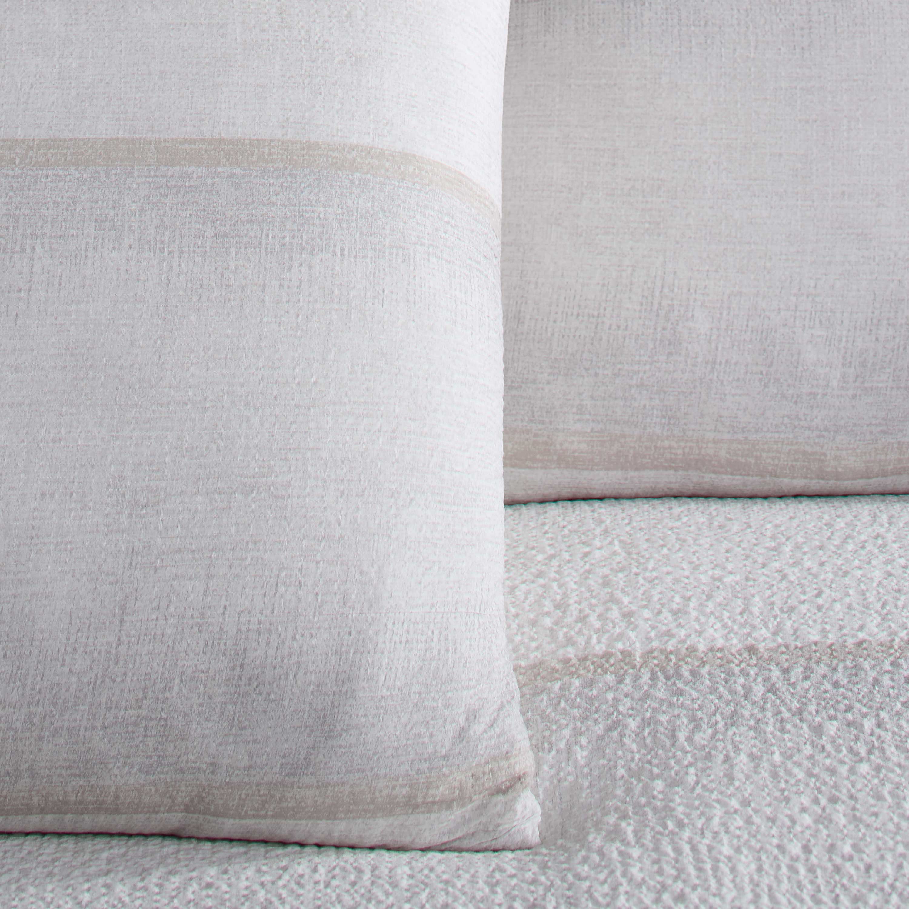 Light-colored comforter set featuring textured fabric and subtle striped design on pillows.