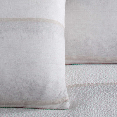 Light-colored comforter set featuring textured fabric and subtle striped design on pillows.