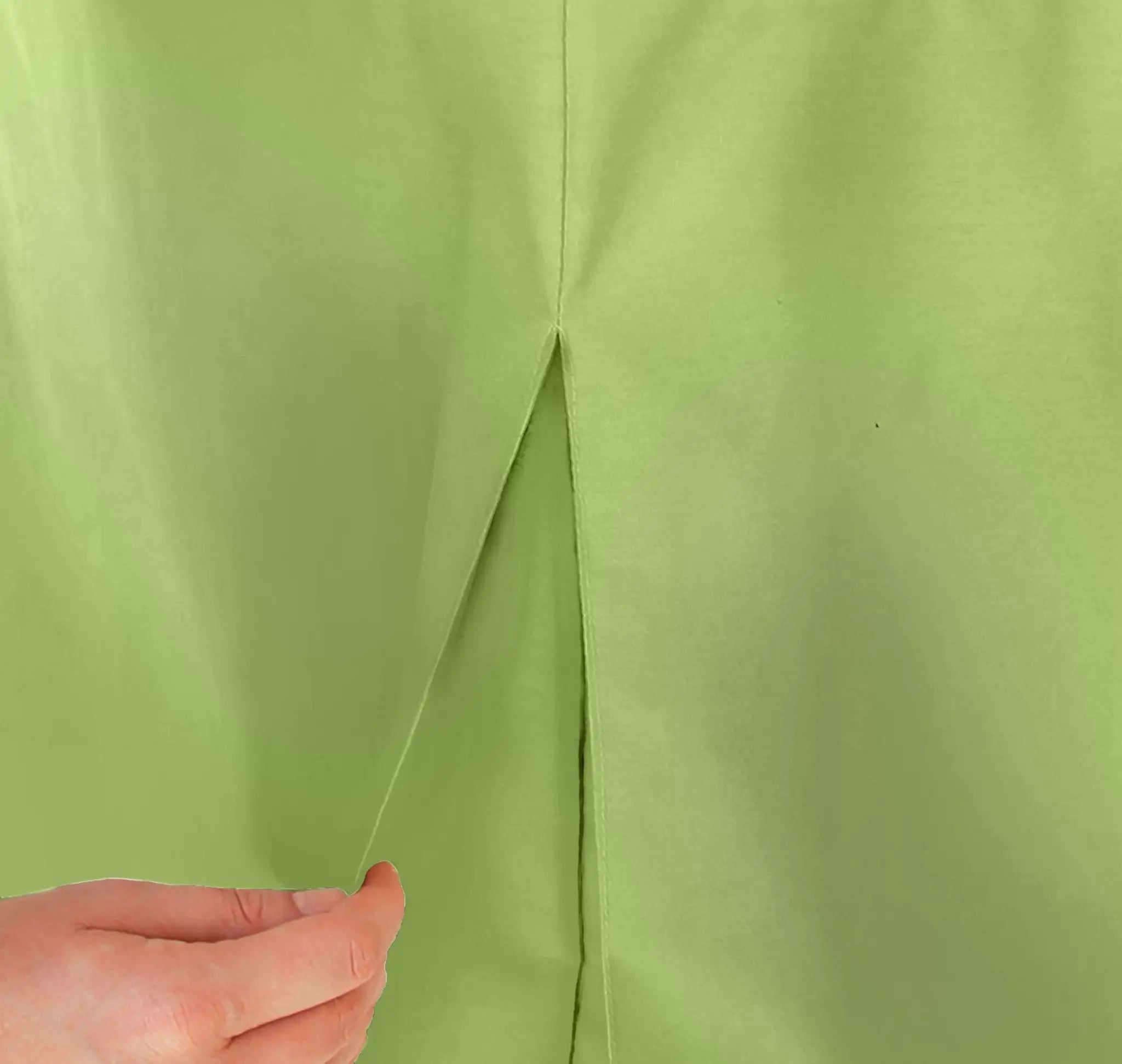 A close-up of a pistachio color table cover, showing a central seam and a hand pulling the fabric apart to demonstrate its stretch.