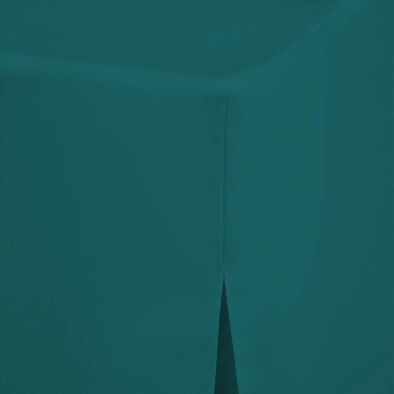 A close-up of a solid teal fabric surface showing a corner fold and a narrow vertical seam.