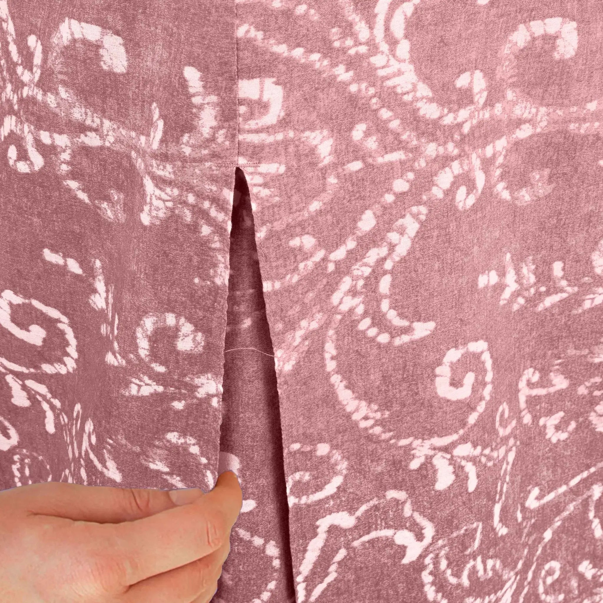 A close-up of a washed red fabric, held open by a hand to show the center seam and texture.