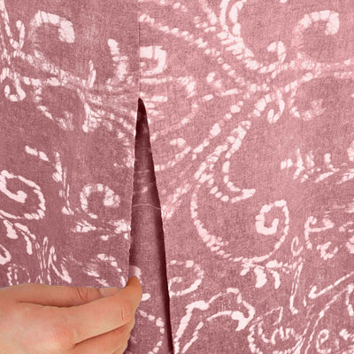 A close-up of a washed red fabric, held open by a hand to show the center seam and texture.