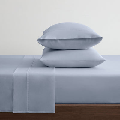 Solid light blue cotton and Tencel sheet set with two stacked pillows on a bed.