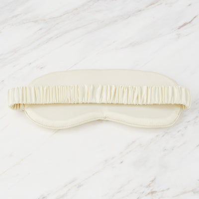 Satin eyemask with a ruffled elastic band, displayed on a marble surface.