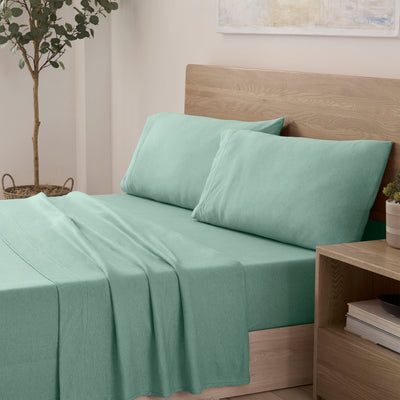 A mint green sheet set is neatly arranged on a bed with two matching pillows and a wooden headboard.