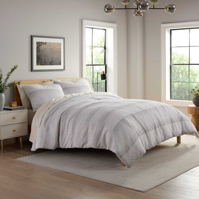 Light gray comforter set on a bed with matching pillows, surrounded by a minimalist bedroom decor.