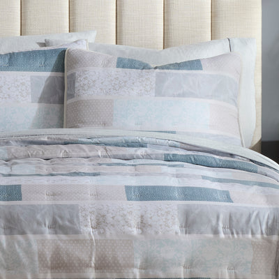 Quilt set featuring a patchwork design in soft blue and neutral tones with matching decorative pillows.