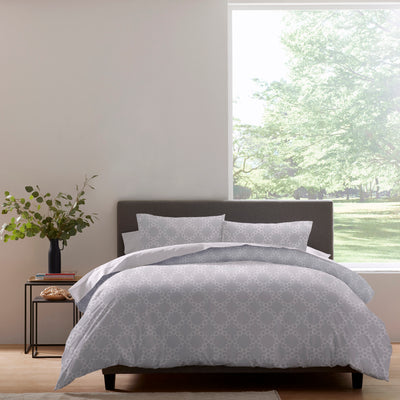 Duvet set featuring a geometric pattern in light gray, displayed on a bed with matching pillows and a plant nearby.