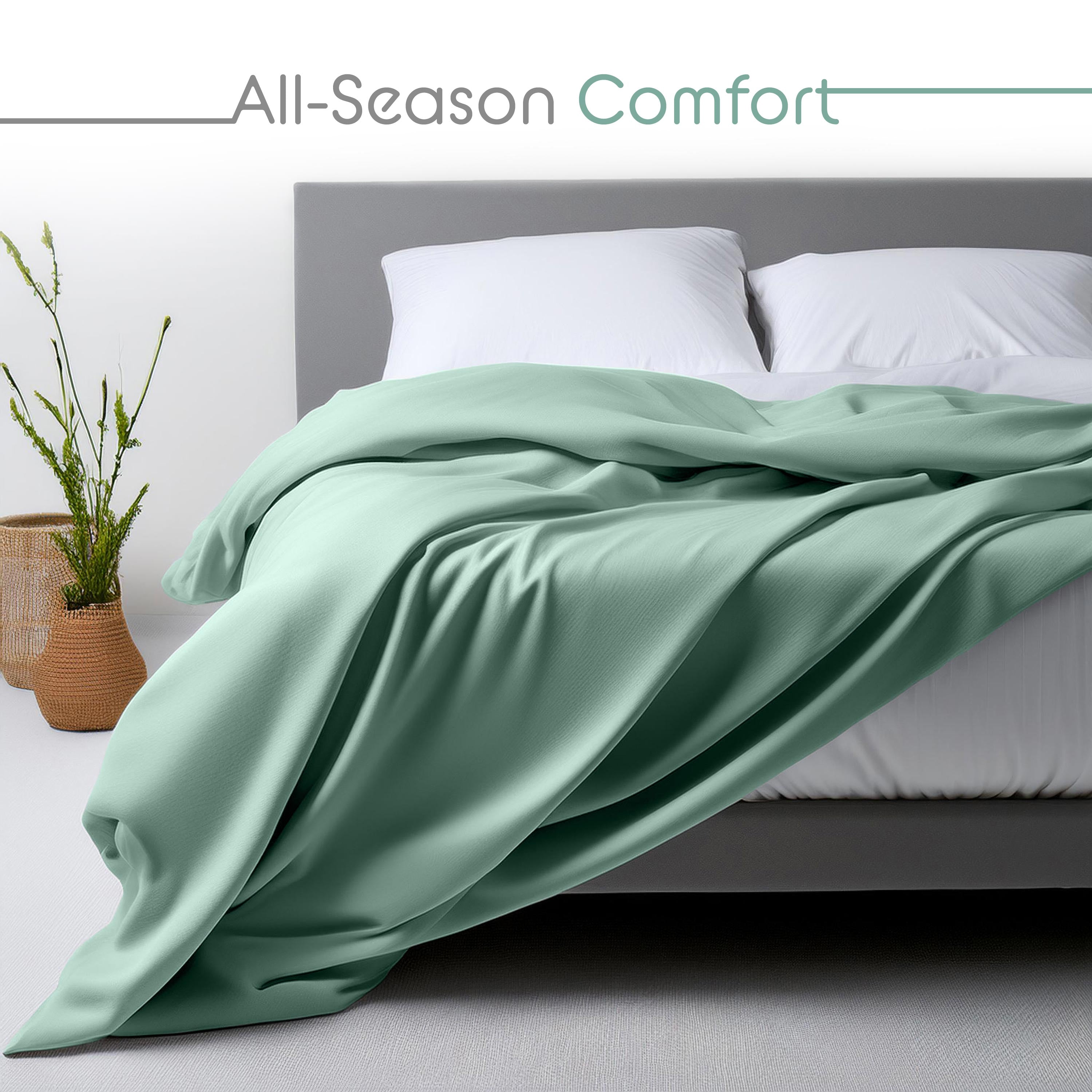 Light green sheet set draped over a bed with white pillows and a decorative plant in a woven basket nearby.