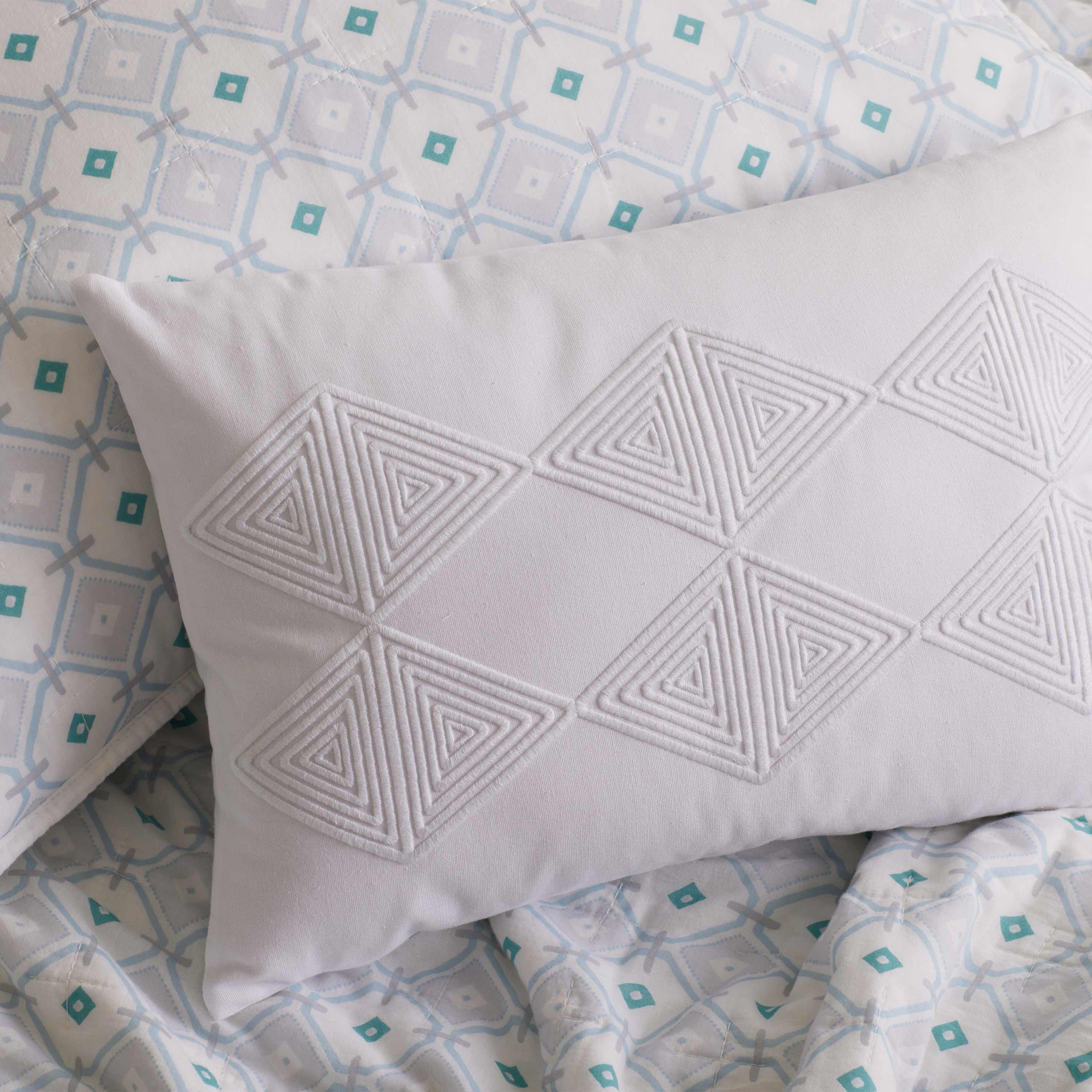 White decorative pillow with textured triangular pattern, placed on a patterned bedding set.