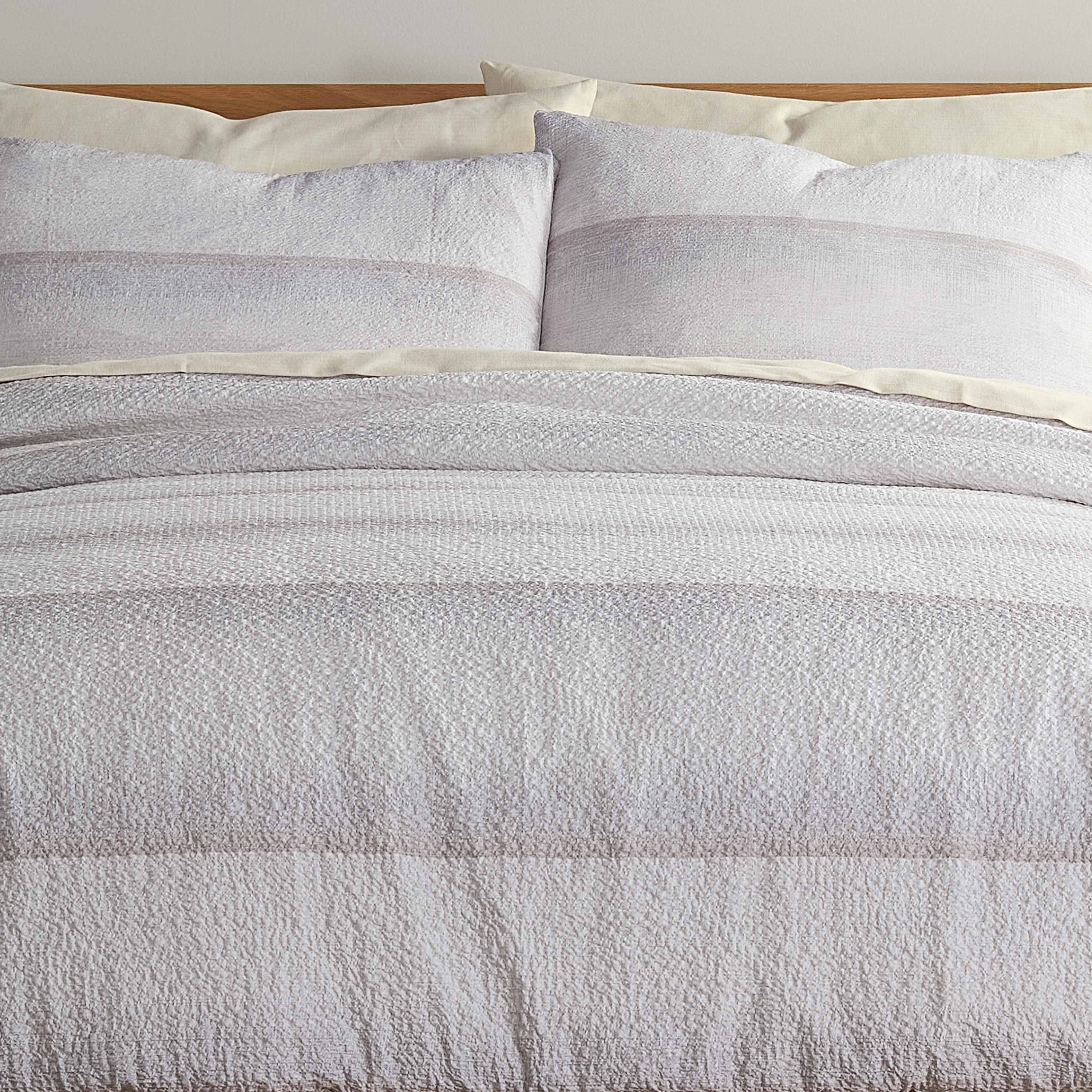 Comforter set featuring a textured light gray design with matching pillow shams on a wooden bed frame.
