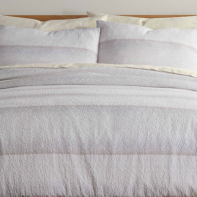 Comforter set featuring a textured light gray design with matching pillow shams on a wooden bed frame.