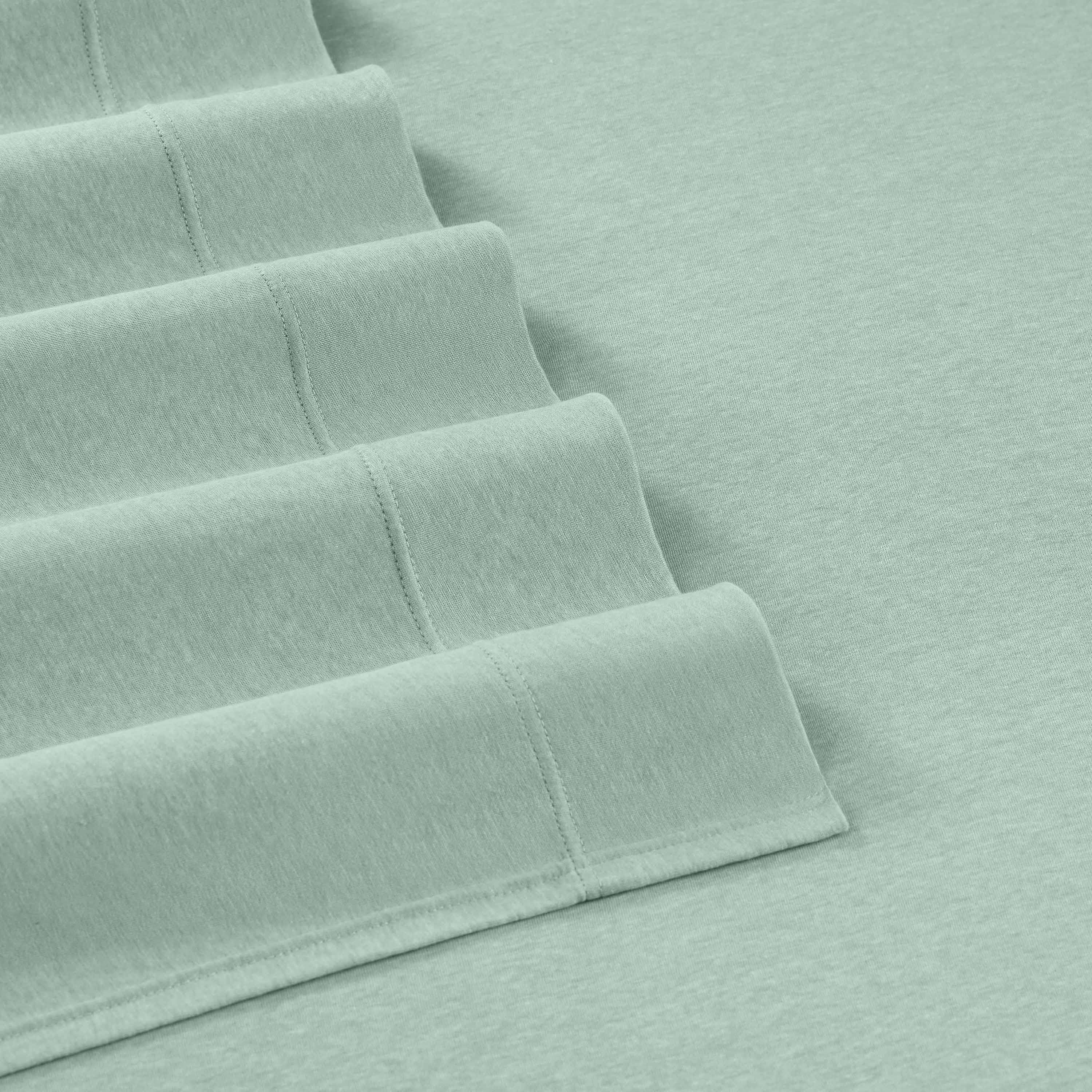 Soft mint green sheets neatly folded, showcasing a smooth texture and stitched edges.