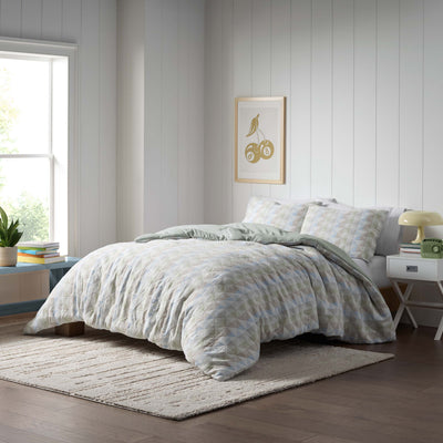 Comforter set with a geometric pattern in soft colors, paired with matching pillow shams on a bed in a bright room.