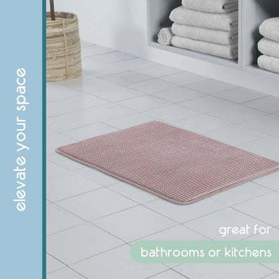 A rectangular berry bath rug shown on a white tiled floor in a bathroom setting. The image includes text overlays reading 'elevate your space' and 'great for bathrooms or kitchens'.
