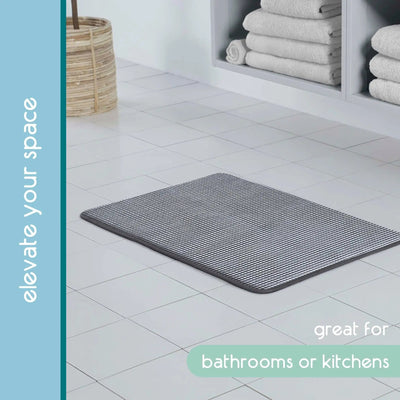 A rectangular black bath rug with a textured striped pattern, shown on a light gray tiled bathroom floor.