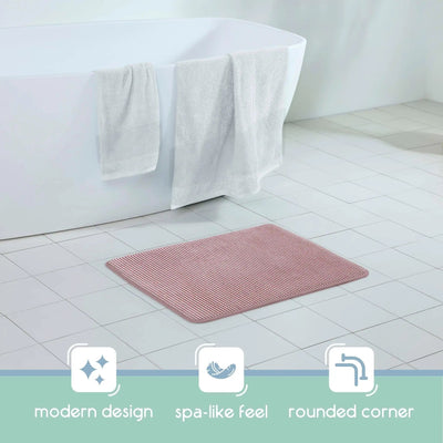 A berry bath rug with rounded corners placed on a white tiled bathroom floor in front of a white bathtub with white towels draped over the edge. Three feature icons and the text 'modern design', 'spa-like feel', and 'rounded corner' appear along the bottom.